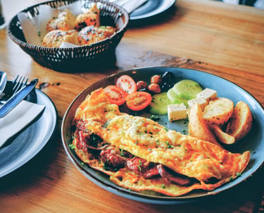 Breakfast plate with a cheese omelette, roasted potatoes, tomatoes, and cucumber slices.