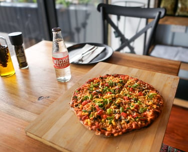 Fresh vegetarian pizza with peppers and corn served on a wooden board next to a cold soda bottle.