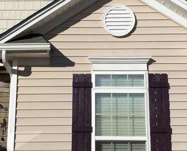 House with two round decorative sections freshly painted white and the shutters freshly painted maroon.