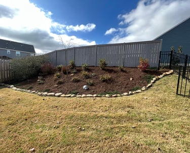 Flower bed on a side hill with various shrubs, brown mulch and large cane rock for a stone border