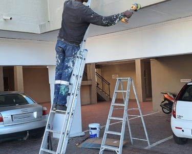 Professional painter on a tall extension ladder painting the exterior facade of a residential building.