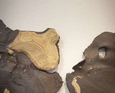 Two abstract hand-formed ceramic sculptures with organic textures and gold leaf accents on a white wall.