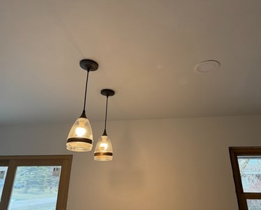 Two modern glass pendant lights hanging from a white ceiling alongside a recessed light fixture.