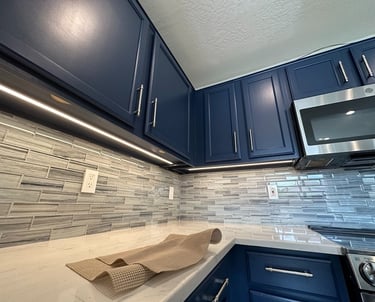 Modern kitchen with navy blue cabinets, white quartz countertops, and LED under cabinet lighting.
