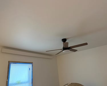 A modern dark wood ceiling fan with light installed on a white bedroom ceiling.