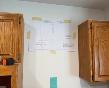 Paper mounting template for range hood installation taped to a kitchen wall between wood cabinets.
