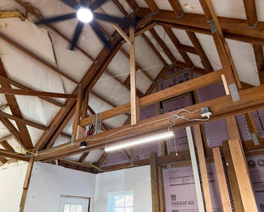 Vaulted ceiling under construction with exposed wood trusses, rigid foam insulation, and a ceiling fan.
