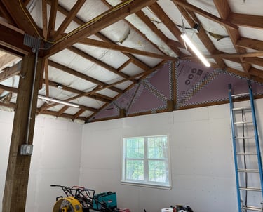 Garage workshop interior with white drywall, exposed wood ceiling trusses, and foam board insulation.