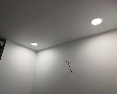 Modern recessed LED ceiling lights illuminating a white wall with exposed electrical wiring.