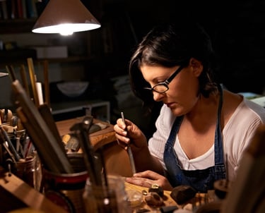 artesana grabando un anillo hecho a mano bajo una lámpara de escritorio en su taller