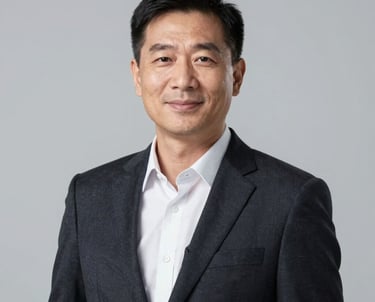 Professional corporate headshot of a business executive in a dark tailored blazer, smiling slightly. Minimalist light gray studio background, soft lighting, professional and highly trustworthy demeanor, Global / North American context.