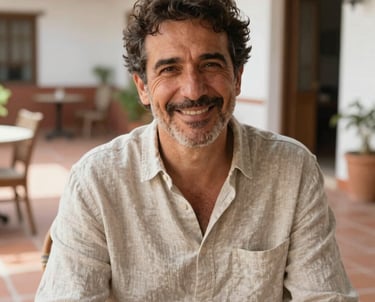 Portrait of a man in his 50s with a kind smile, looking relaxed and satisfied, wearing a linen shirt, set in a bright patio with terracotta tiles in a Spanish-speaking region.