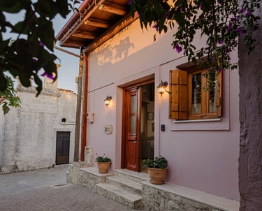 Charming cottage entrance: soft pink exterior, wooden doors, vibrant purple flowers