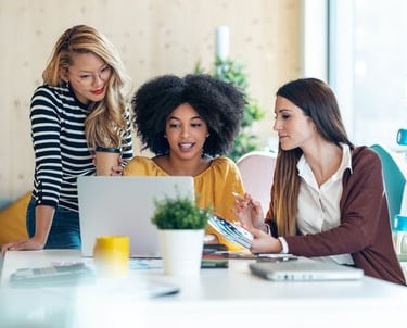 three women sitting at a table viewing a laptop