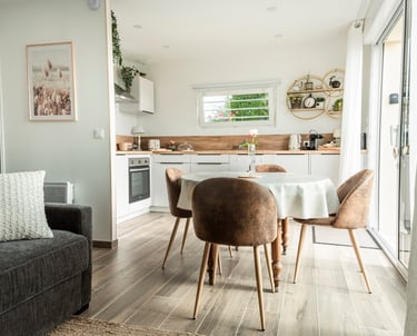 Modern open plan studio apartment featuring a white kitchen, dining table with brown chairs, and cozy living area.