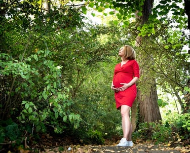 Photo d'une femme enceinte vêtue d'une robe rouge, debout dans une zone boisée
