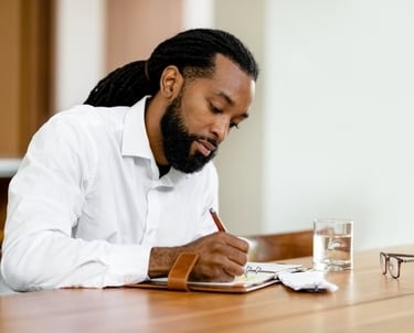 a man in a white shirt and glasses is writing in a journal