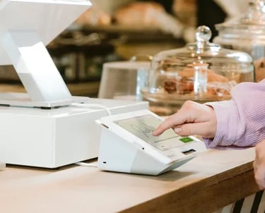 Customer using a touchscreen POS terminal to sign for a digital payment at a cafe counter.