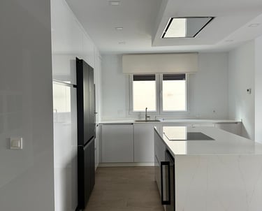 Cocina blanca, isla, electrodomésticos negros, suelo madera.