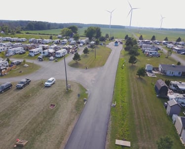 Aerial view of a spacious RV park and campground featuring paved roads, trailers, and wind turbines.