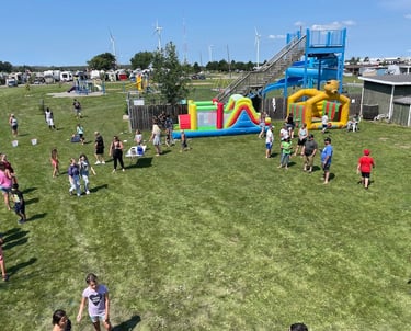 Families enjoy a summer festival at an RV park with inflatable bounce houses and a water slide.