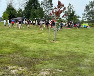 A large group of people participating in outdoor activities at a grassy summer camping retreat.