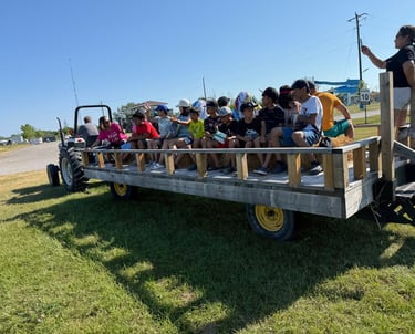 A group of children enjoying a tractor-pulled hayride on a sunny farm field during a summer outing.