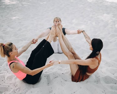 Photo des trois professeurs assises, se tenant les mains en cercle, les pieds connectés vers le ciel