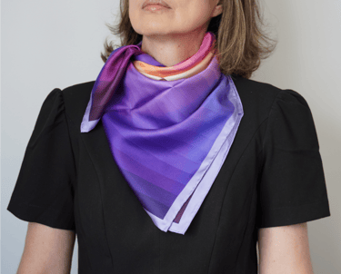 Lenço de seda colorido em tons de lilás e laranja no pescoço e mulher com roupa preta.