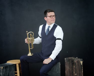 A man in a vest and tie is holding a cornet, looking to the side.