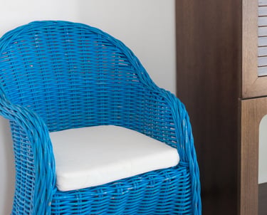 a wicker chair with a blue chair and a cabinet