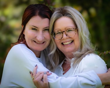Two happy women in white shirts smiling and hugging outdoors with a soft blurred background. Athens