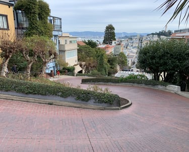 A winding brick road on Lombard Street in San Francisco with city views and lush gardens.