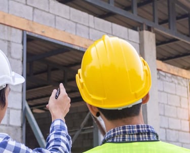 two men in hard hats and safety vests are standing in front of a building
