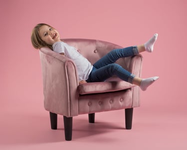 Enfant sur un fauteuil rose qui rit et lève les pieds, sur fond rose