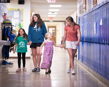 a group of children holding hands and walking down a hallway