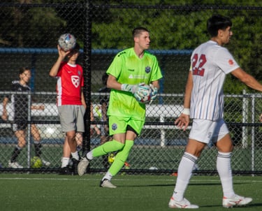 Midlakes goalkeeper with ball in hand looking to play it. Opposing player in foreground.