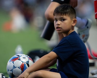 Ball boy sitting with a soccer ball.