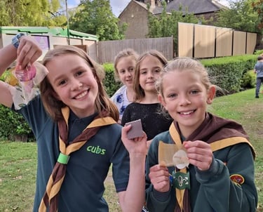 Two smiling Cub Scouts proudly showing materials from an outdoor activity, with other Cubs behind th
