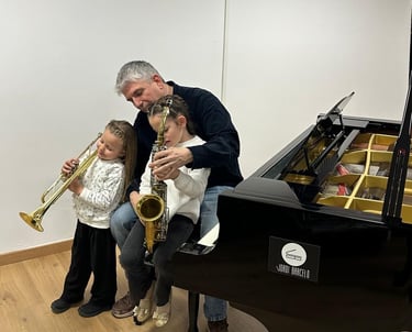 two little girls playing with a trumpet and saxophone infront a baby piano and music teacher
