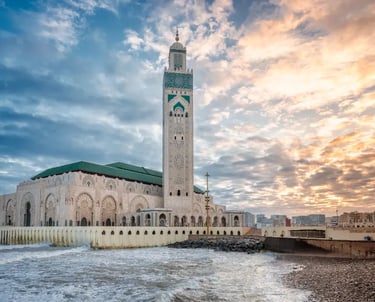 The Hassan II Mosque in Casablanca, Morocco, sits on the Atlantic coast under a sunset sky.