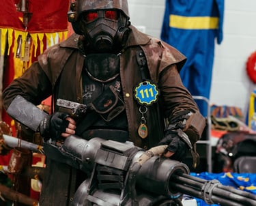 A man in a Fallout game costume stands with a large prop weapon and mask