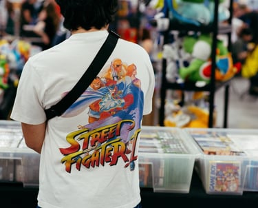 A man wearing a street fighter video game shirt looks at games for sale