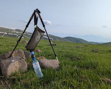 A water bladder is suspended between two trekking poles filtering water through a sawyer squeeze.
