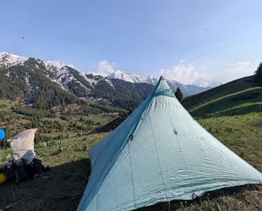 Lightweight Hyperlite Ultamid tent pitched on a grassy mountain ridge overlooking snow-capped peaks.