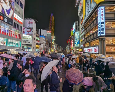 A crowd of people with umbrellas in Dotonbori, Osaka on a dark and rainy October night.