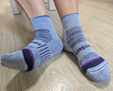 Samantha's feet wearing gray moisture-wicking Wrightsocks performance crew socks on a wooden floor.