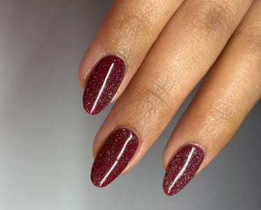 Image of perfectly manicured hands with burgundy nails with sparkles in them