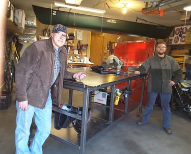 Two Welders standing by a welding table