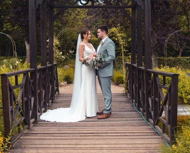 Brautpaar steht verliebt auf einer Holzbrücke im Grünen. Romantische Hochzeitsfotografie von Just Perspectives.